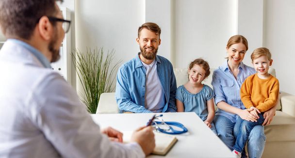 Szczęśliwi rodzice i dzieci siedzący na sofie i komunikujący się z lekarzem podczas wizyty we współczesnym clini - Zdjęcie, obraz