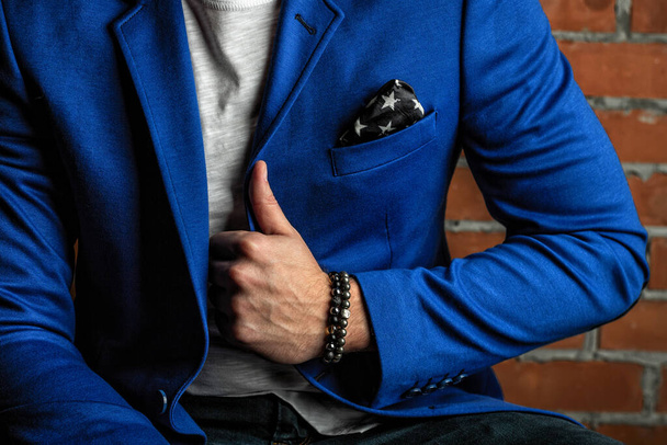 Pulseiras cromadas feitas de pedras preciosas e minerais à mão, em um terno de negócios azul em um fundo de parede de tijolo
 - Foto, Imagem
