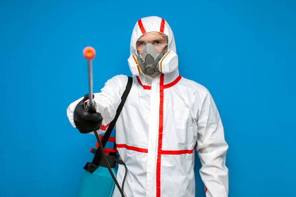 odporność na koronawirus. pracownik dezynfekcji w kombinezonie ochronnym i respiratorze posiada spray chemiczny, wirusolog na niebieskim odizolowanym tle - Zdjęcie, obraz