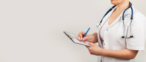 Vrouwelijke arts schrijft met een pen een document op een tablet, schrijft een medische geschiedenis. Het concept van gezondheidszorg, geneeskunde - Foto, afbeelding