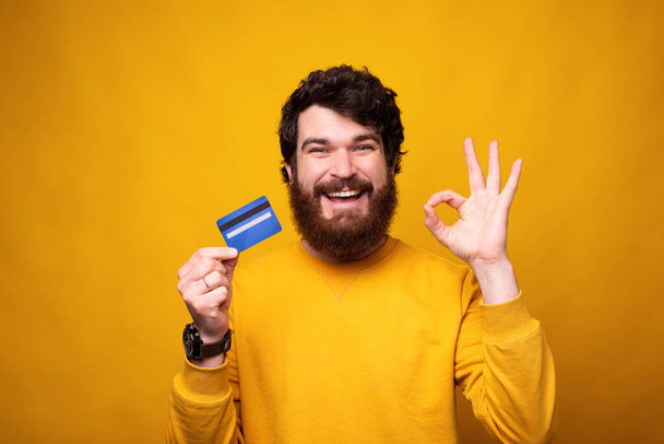 Jovem barbudo homem está fazendo ok gesto enquanto segurando um cartão
. - Foto, Imagem