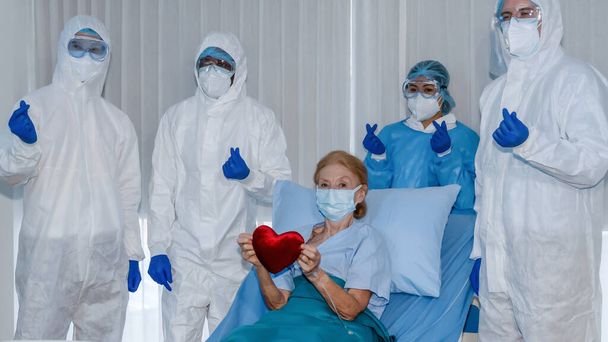 Kaukasische senior coronavirus covid-19 geïnfecteerde patiënt liggend op bed in quarantaine kamer in het ziekenhuis met arts en medisch team poseren voor fotografie samen na patiënt herstellen van desease - Foto, afbeelding
