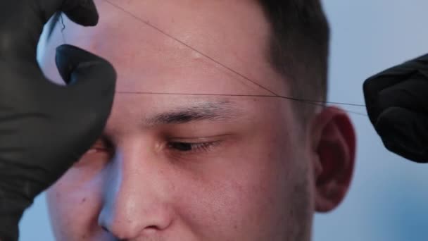 Browist makes eyebrow correction with a thread to a man in a beauty salon. - Footage, Video