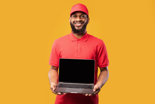 Dodací muž drží notebook s prázdnou obrazovkou stojící ve studiu - Fotografie, Obrázek