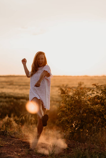 Joven mujer hermosa haciendo polvo con el pie y gritando en el campo de trigo naranja en un día soleado de verano. Enloqueciendo. Sentirse libre y feliz. Esperanza milagrosa. Puesta de sol en aislamiento. Deslumbramiento solar
 - Foto, Imagen