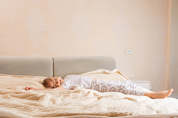 Красивая маленькая девочка в пижаме лежит на кровати дома. Оставайтесь дома во время коронавируса covid-19 и веселитесь
. - Фото, изображение