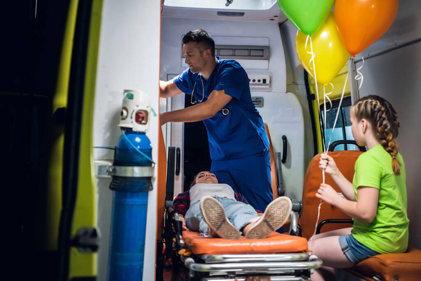 Madre priva di sensi sdraiata su una barella in un'ambulanza, un paramedico che le fornisce il primo soccorso - Foto, immagini