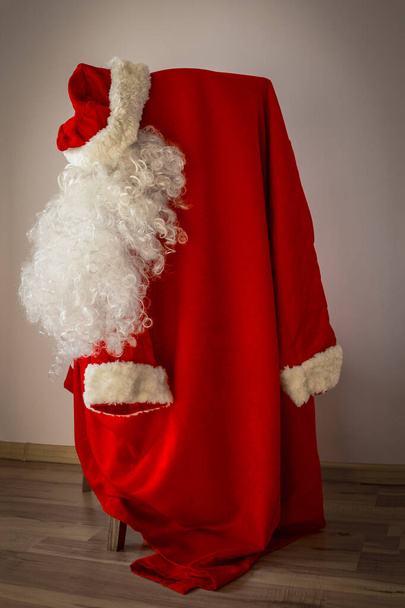 Kostým Santa Clause visí na židli. Bílý plnovous, červený klobouk a kožich. Světlé pozadí, vinětace. Svislé uspořádání. - Fotografie, Obrázek