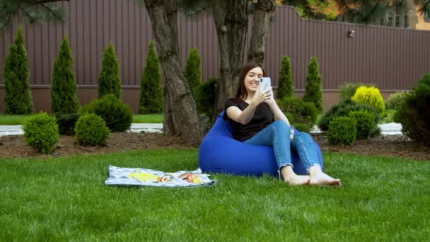 Young woman having video call in garden - Materiał filmowy, wideo