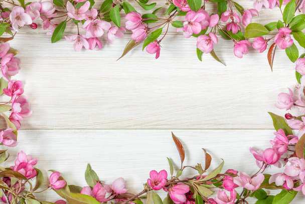 Rózsaszín virágok egy dekoratív almafa egy könnyű fa asztalon. Virágkeret. Kép a gratulációk tervezéséhez, naptár a tavasz témájához. - Fotó, kép