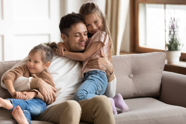 Liefdevolle jonge vader knuffelend met twee kleine dochters - Foto, afbeelding