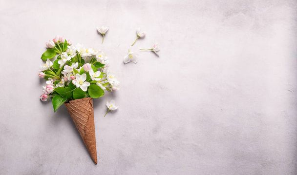 Flowers twig blossoming apple tree sakura waffle cone ice cream on a gray concrete background. Horizontal frame top view - Foto, immagini