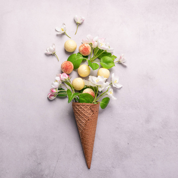 White chocolate truffle candy flowers waffle cone ice cream on gray concrete background. Square frame copy space. - Photo, Image