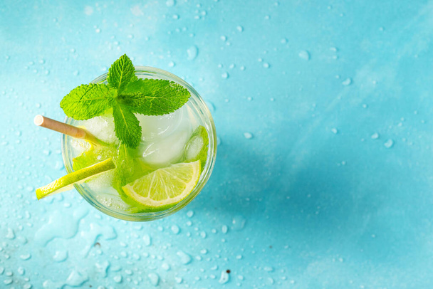 Domácí limonáda nebo mojito koktejl s citrónem, mátou a kostkami ledu ve sklenici na lehkém kamenném stole. Čerstvý letní drink. Horní pohled s mezerou pro kopírování - Fotografie, Obrázek