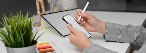 Boční pohled návrhářky pracující s modelovým tabletem při hledání informací o horizontálním modelovém smartphonu  - Fotografie, Obrázek