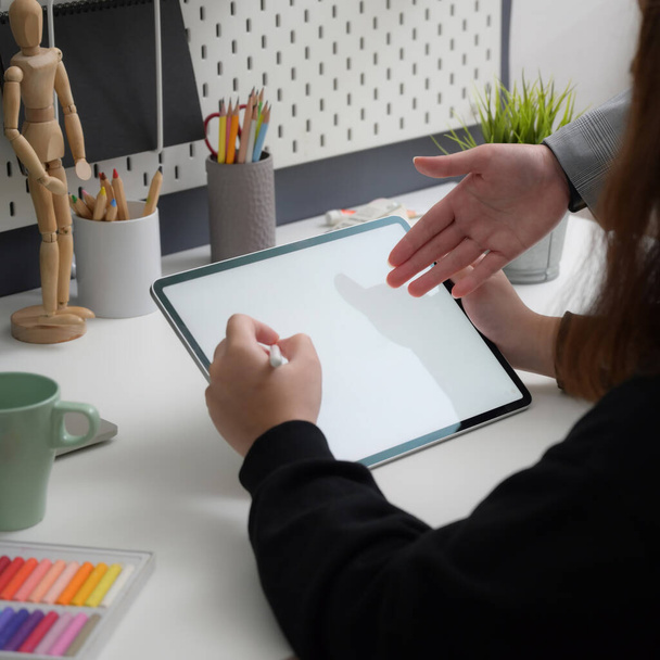 Close up view of female designer working on mock-up tablet with stylus pen while consulting with her colleague in trendy workplace - Foto, imagen