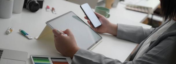Boční pohled profesionálního designéra pracujícího na maketovém smartphonu a tabletu na bílém stole s designérskými potřebami  - Fotografie, Obrázek