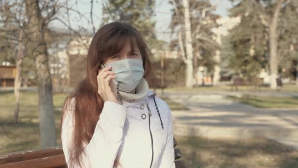 free young woman in a medical protective mask is sitting with a smartphone on city street in Europe. healthy girl tourist on street wear protective mask from viruses. concept health. - Footage, Video