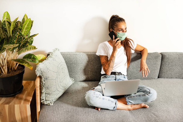 young woman working at home in face mask in room sofa background - Φωτογραφία, εικόνα