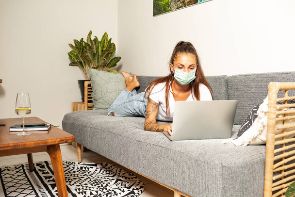 young woman working at home in face mask in room sofa background - Фото, зображення
