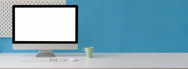Close up άποψη του δημιουργικού χώρου εργασίας με κενό υπολογιστή οθόνη, κούπα και αντίγραφο χώρο στο λευκό τραπέζι με ράφι σε γαλάζιο τοίχο - Φωτογραφία, εικόνα