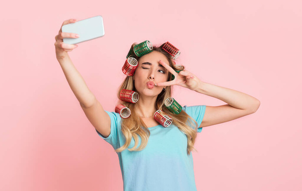 Social networks for housewife concept. Girl in curlers, make blowing kiss for selfie - Foto, immagini