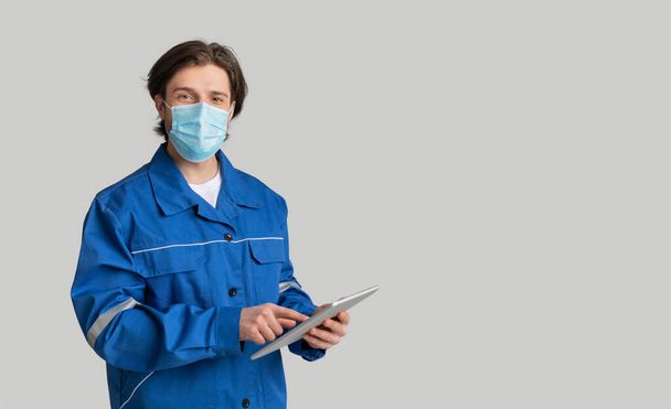 Młody inspektor ilościowy noszący maskę medyczną i korzystający z tabletu cyfrowego - Zdjęcie, obraz