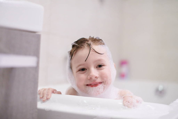 little girl playing with soap foam in bath during coronavirus stay at home pandemic quarantine - Valokuva, kuva