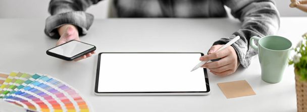 Gesneden foto van vrouwelijke ontwerper die werkt aan haar project met blanco scherm tablet, smartphone en ontwerper levert thuis kantoor - Foto, afbeelding