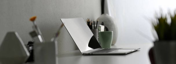 Widok z boku nowoczesne biurko z laptopem, narzędzia do malowania i dekoracje na białym stole - Zdjęcie, obraz