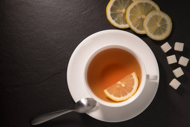 Imagen vista superior de una taza de té con limón sobre fondo de granito negro
 - Foto, Imagen