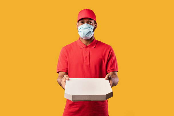Futár Guy holding Pizza doboz visel maszk sárga háttér - Fotó, kép