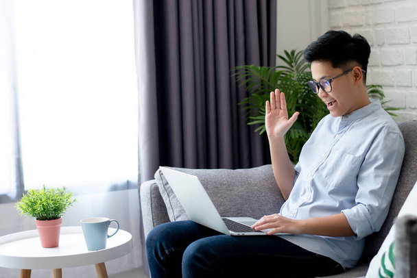 Молодые азиаты работают на ноутбуках с видеозвонками для встреч и сидят дома на диване
. - Фото, изображение