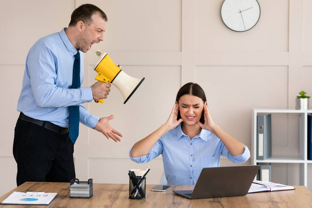 Boze zakenman schreeuwt tegen vrouwelijke werknemer houdt Megaphone in Office - Foto, afbeelding