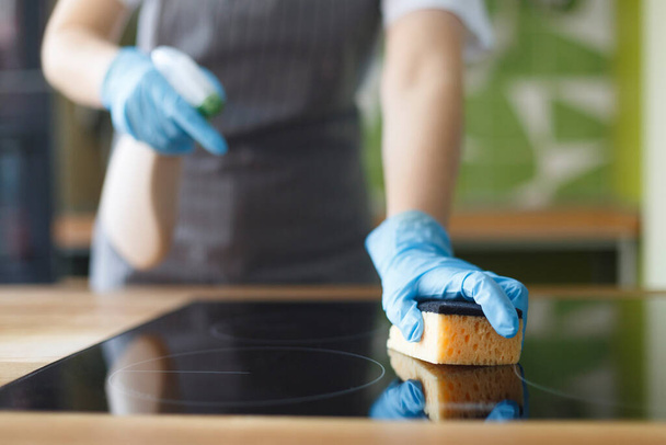 Mujer en delantal puliendo la encimera de la cocina con un aerosol
 - Foto, Imagen