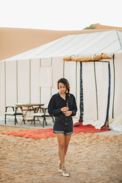 Muoti tyylikäs muotokuva nuorten itämainen brunette nainen mustissa vaatteissa. Seisoo lähellä glamping teltta Saharan autiomaassa luksusleirillä, Marokko
. - Valokuva, kuva