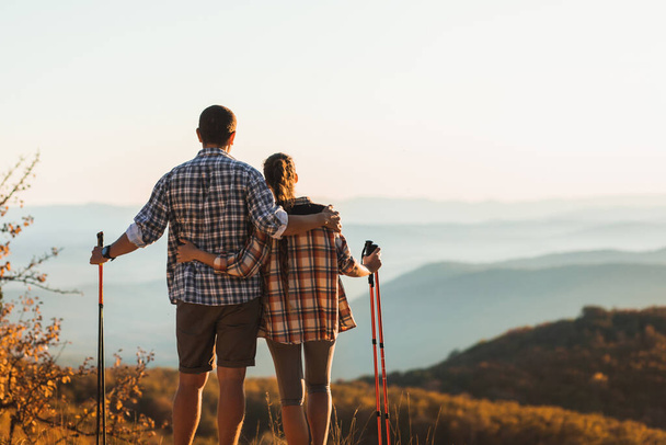 Couple hiking in autumn mountains with trekking sticks. Nordic walking outdoors, view from behind. Travel lifestyle. - Photo, Image