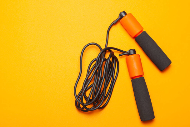 Скакалка. Забавные упражнения для здоровья тела. Оранжевая веревка с черным. Жёлтый фон
 - Фото, изображение