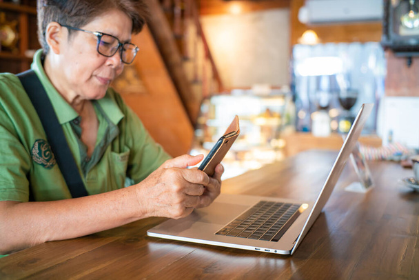 シニアアジアの女性は、コーヒーショップのビジネス女性の仕事にノートパソコンに座ってスマートフォンを使用します - 写真・画像
