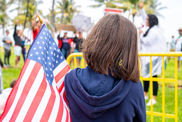 Amerikai zászló és gyerek a bemutatón. Kis hazafi. Az amerikai zászlós lány. Amerikai gyerekek. Egy gyermek tiltakozik a koronavírus-korlátozások ellen. Miami tüntetők. Polgári jogok. A demokrácia. - Fotó, kép