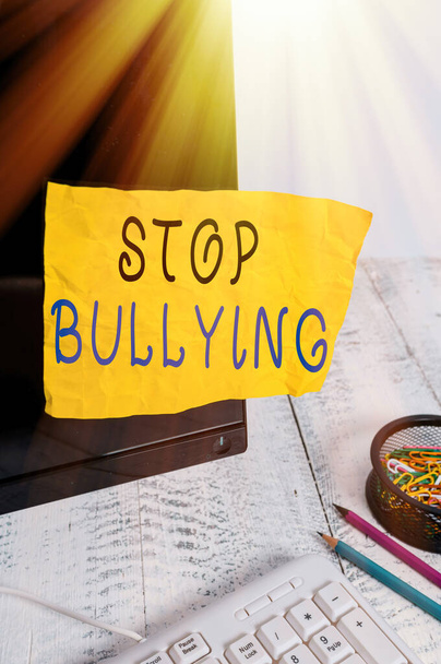 Text sign showing Stop Bullying. Conceptual photo Fight and Eliminate this Aggressive Unacceptable Behavior Note paper taped to black computer screen near keyboard and stationary. - Foto, Imagen