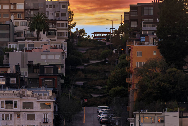Yüksek açı San Francisco, Kaliforniya 'daki ünlü eğri büğrü Lombard Caddesi tepenin üstünde ikonik bir teleferik ve gün batımında sıcak gökyüzü. - Fotoğraf, Görsel