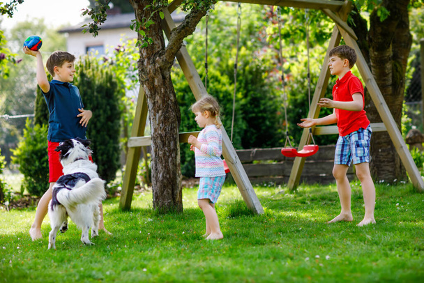 Dos chicos y una niña jugando con un perro de la familia en el jardín. Tres hijos, hermanos adorables divirtiéndose con el perro. Familia feliz al aire libre. Amistad entre animales y niños - Foto, Imagen