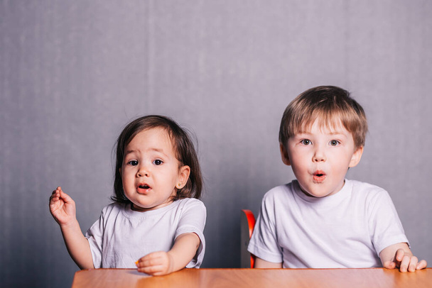 Kleine jongen en klein meisje zeer verrast zitten aan de tafel, kleuterschool kinderen - Foto, afbeelding
