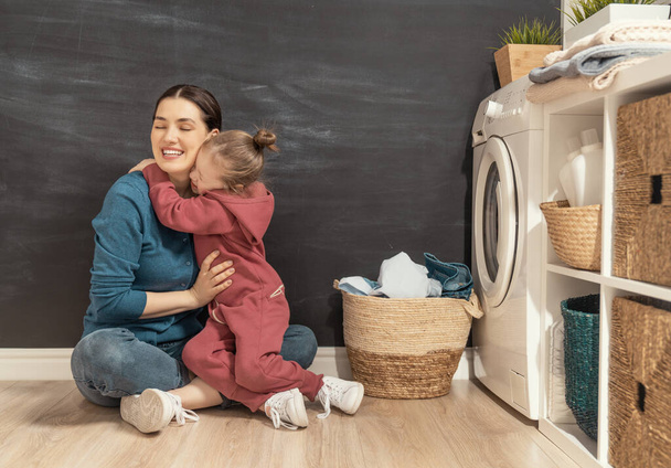 Beautiful young woman and child girl little helper are having fun and smiling while doing laundry at home.   - Foto, Bild