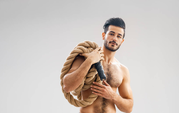 Athletic young man doing crossfit exercises with a rope on grey background. - Φωτογραφία, εικόνα