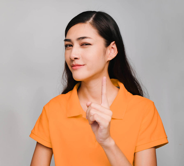 young beautiful asian woman,long black hair, wore orange t shirt, Pointing finger forward, Show a question remind face,Don't forget, on gray background - Foto, Bild