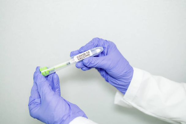 Primer plano de la mano del microbiólogo o del trabajador médico con guantes quirúrgicos azules que sostienen un recipiente que contiene una jeringa con la vacuna para el Coronavirus de rápida propagación. Concepto de vacuna COVID-19
 - Foto, imagen