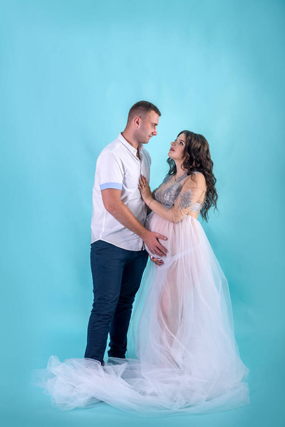 geweldig zwanger paar poseren in studio tegen diep blauw achtergrond, wachten op een baby - Foto, afbeelding