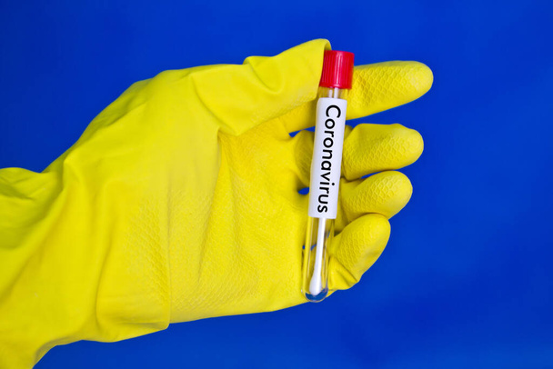 Hand in yellow medical rubber gloves holding test tube with red blood on blue background with the inscription coronavirus. - Fotografie, Obrázek